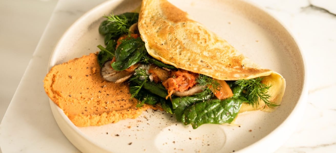 A golden brown omelette on a white plate, filled with fresh green vegetables